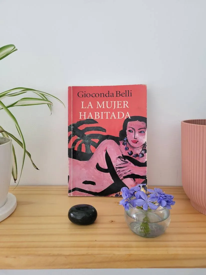 El libro La mujer habitada de Gioconda Belli, junto a flores y una piedra