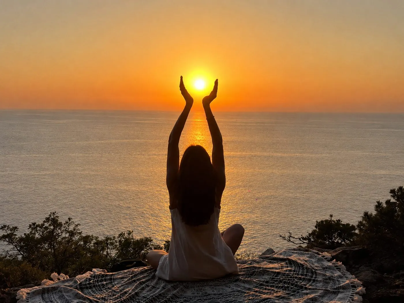 Práctica de yoga frente al mar al atardecer, sosteniendo el sol entre las manos
